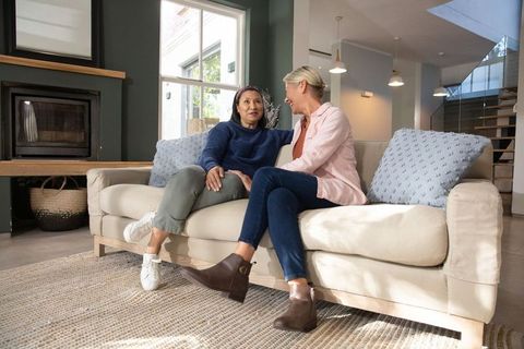 Middle-aged female couple conversing and smiling on sofa in modern cozy living room
