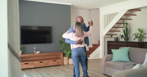 Diverse couple dancing in cozy modern living room embracing near stairs and plants