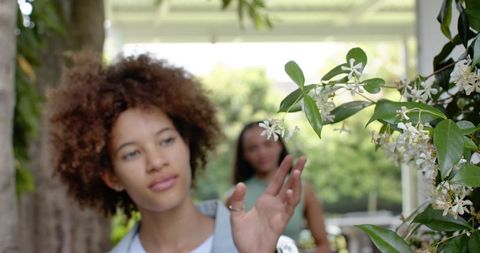 African american friends reaching toward white jasmine blossoms on sunny porch