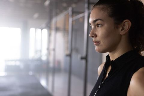 Woman gazing in gym wearing black zip-top near metal rig backlit portrait