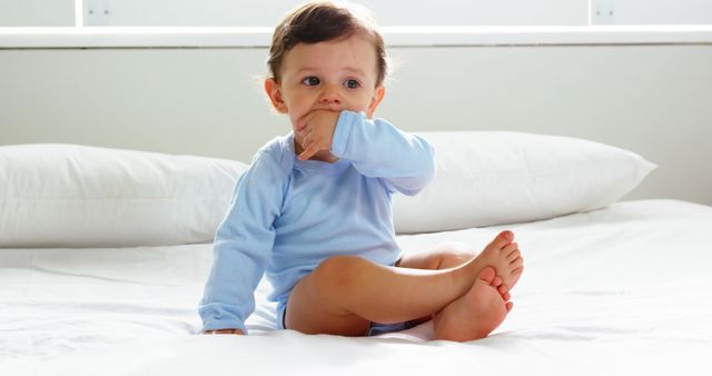 Cute baby with nightwear sitting on a bed at home