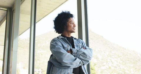 Contemplative african american man in denim jacket looking out glass window at hillside view