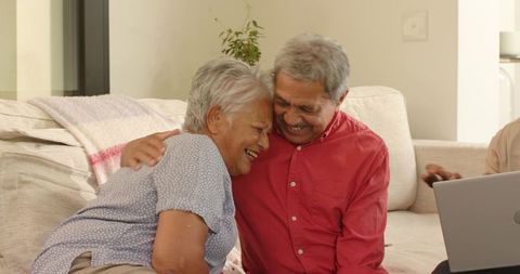 Senior Couple Laughing and Embracing on Sofa with Laptop in Cozy Living Room