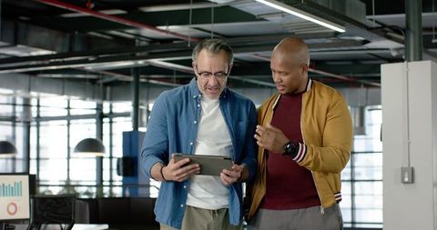 Diverse colleagues collaborating over tablet in modern loft office with casual attire
