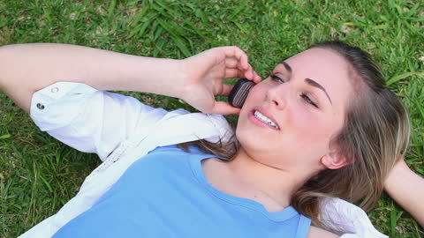 Happy Woman Talking on Phone While Relaxing on Grass