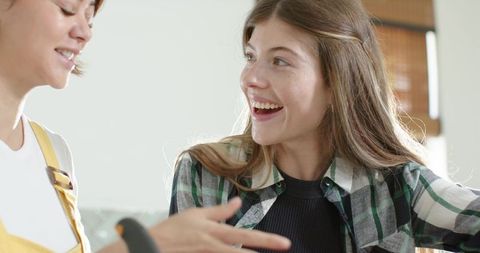 Young women laughing and chatting in bright kitchen wearing plaid shirt and yellow apron