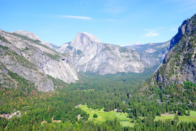 A captivating scene of Yosemite Valley showcasing the iconic mountain peaks, dense forests, and wide-open green spaces under a clear blue sky. Ideal for promoting travel destinations, nature magazines, outdoor adventure advertisements, and environmental conservation campaigns.