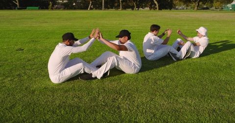 Diverse male cricketers performing partnered sit-up drills on sunlit grass field team training