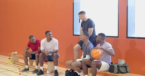 Diverse male basketball team packing gear and walking toward court after pep-talk