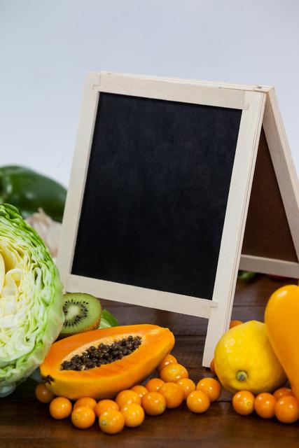 Close-up of chalkboard surrounded with fresh vegetables and fruits