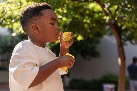 African american boy blowing soap bubbles in sunlit garden, playful summer childhood