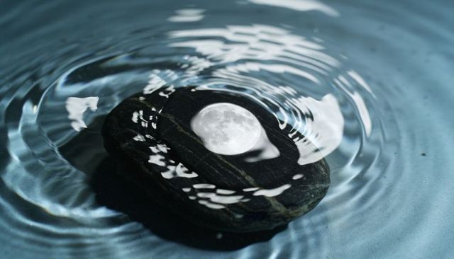 Moon reflection on black river stone with ripples creating surreal zen nightscape