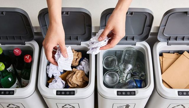 Hands sorting recyclables into sensor-operated bins featuring glass bottles paper envelopes
