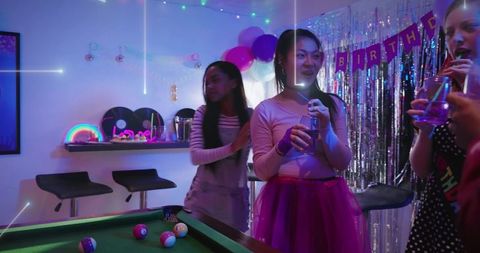 Teen celebrating birthday holding drink wearing tulle skirt at neon living room party