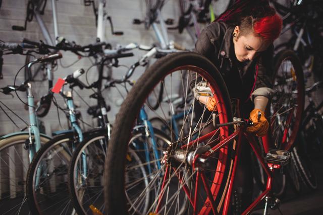 This shows a young female mechanic with red hair repairing a bicycle in a workshop filled with various bikes. Perfect for use in promotions related to bike repair services, female empowerment in trades, professional mechanics, or cycling enthusiasts. Can be used in blogs, websites, or advertisements highlighting bike maintenance and repair.
