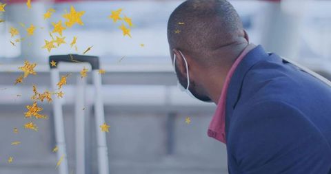 Businessman wearing mask waiting at airport terminal near suitcase and gold star confetti