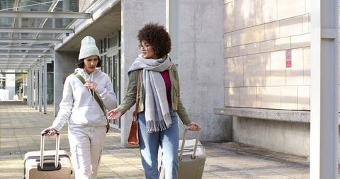 Two women walking with hard-shell luggage along modern urban glass-canopy walkway