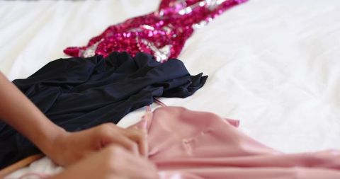 Selecting evening dresses on bed: pink satin slip, black gown, sequined magenta dress