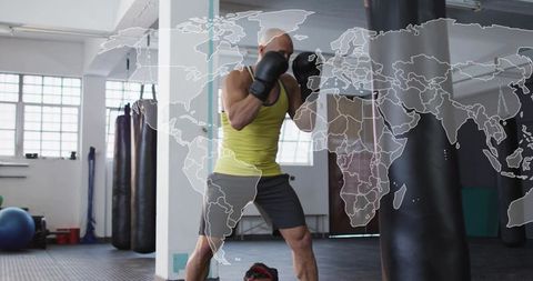 Bald boxer training with heavy bag in bright gym with world map overlay