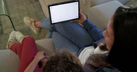 Mother and Child Watching Tablet Together at Home on Couch Holding Blank Screen for Mockup
