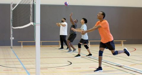 Diverse male teammates practicing volleyball drill, passing ball on indoor gym court near net