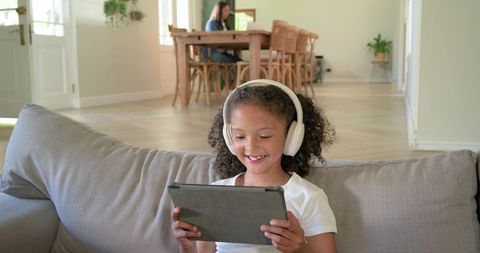Smiling child using tablet with wireless headphones in bright open-plan living room