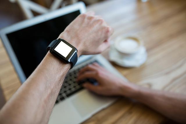 Close-up of hand wearing smartwatch using a laptop in coffee shop