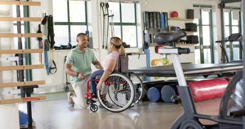 Kneeling Therapist Assisting Wheelchair User During One-on-One Rehabilitation Session