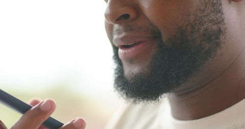 African man speaking into smartphone near window soft light closeup beard fingertips