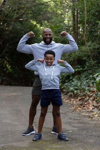 African american father and son flexing muscles on forest trail wearing matching hoodies