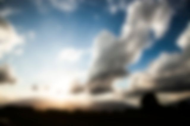 Blurry image of a landscape with dramatic cloud formation and sunset in background. Ideal for use in projects conveying calmness, peacefulness, or abstract art. Suitable for backgrounds, advertisements, and nature-themed designs.