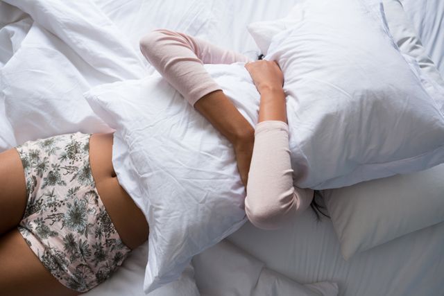 Woman holding pillow while relaxing on bed at home