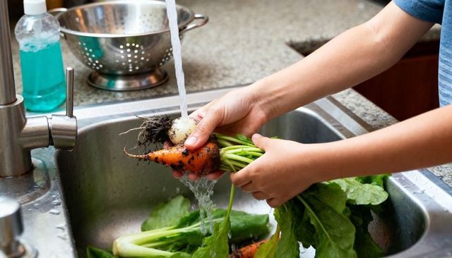 Rinsing fresh root vegetables under running kitchen faucet with leafy greens and soil