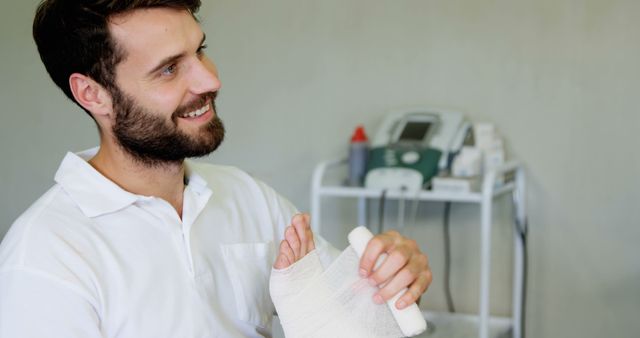 Man smiling while treating hand injury with bandage in clinic - Download Free Stock Images Pikwizard.com