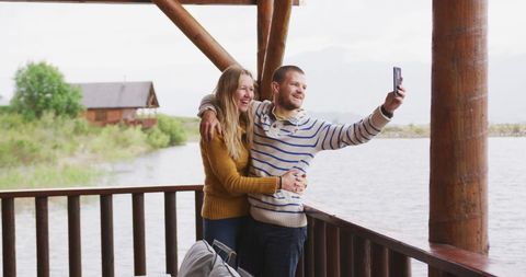 Smiling Couple Taking Selfie at Scenic Lakeside Cabin Getaway