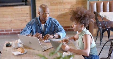 African american coworkers collaborating in coffee shop, reviewing reports on laptops
