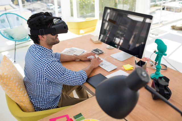 Graphic designer in virtual reality headset working on computer at desk in the office