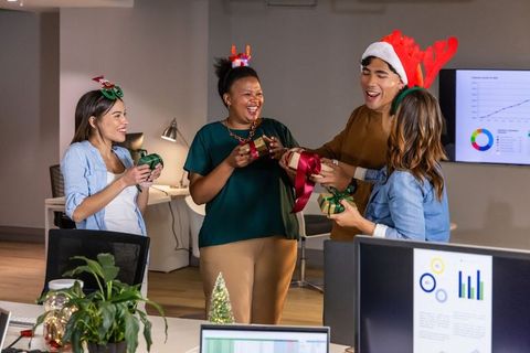 Multicultural office team celebrating holiday gift exchange in festive hats and laughter