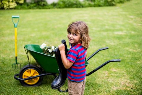 Joyful child gardening with rubber boots in lush backyard