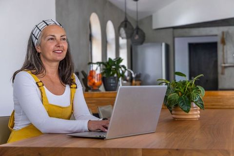 Senior woman working remotely on laptop at modern kitchen island, relaxed home office