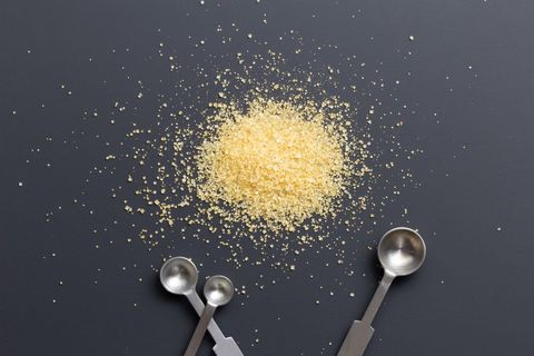 Granulated cane sugar with metal measuring spoons on dark background
