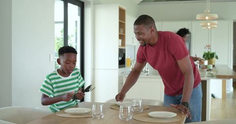 African american family arranging dining table in modern sunlit kitchen