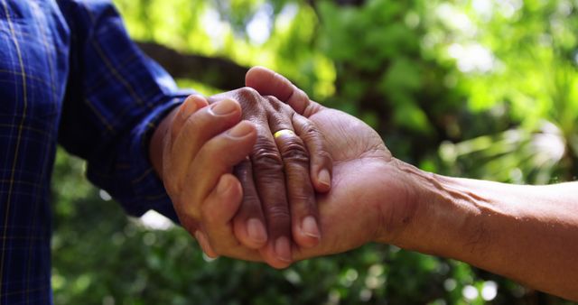 Two individuals are holding hands in a gesture of support or partnership, with copy space. Their clasped hands symbolize trust, friendship, or a mutual agreement in a natural outdoor setting.