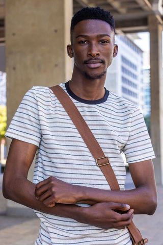 Confident african american man in urban plaza wearing striped tee and crossbody bag