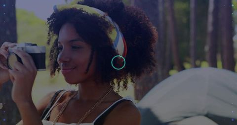 Young woman capturing campsite memories with vintage camera and colorful headband