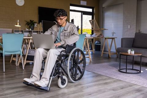 Indian man working on laptop in wheelchair in modern coworking lounge