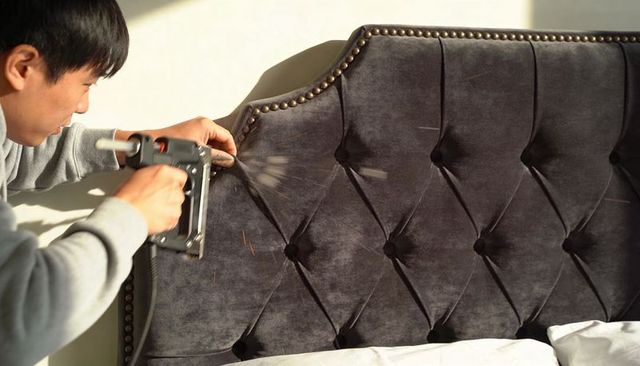 Upholsterer fastening tufted velvet headboard with staple gun close-up craftsmanship