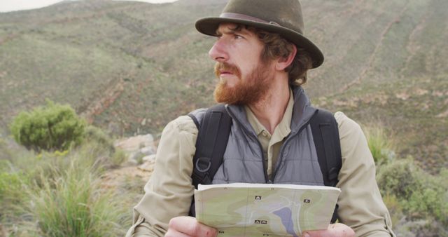 Bearded caucasian male survivalist on mountain in wilderness, reading map and looking around. exploration, travel and adventure, survivalist in nature.