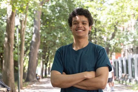 Confident african american man standing with arms crossed smiling on tree-lined urban path