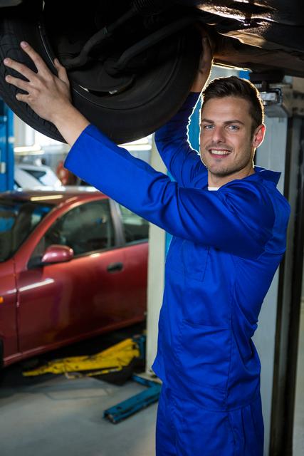 Portrait of happy mechanic fixing a car tyre at repair garage